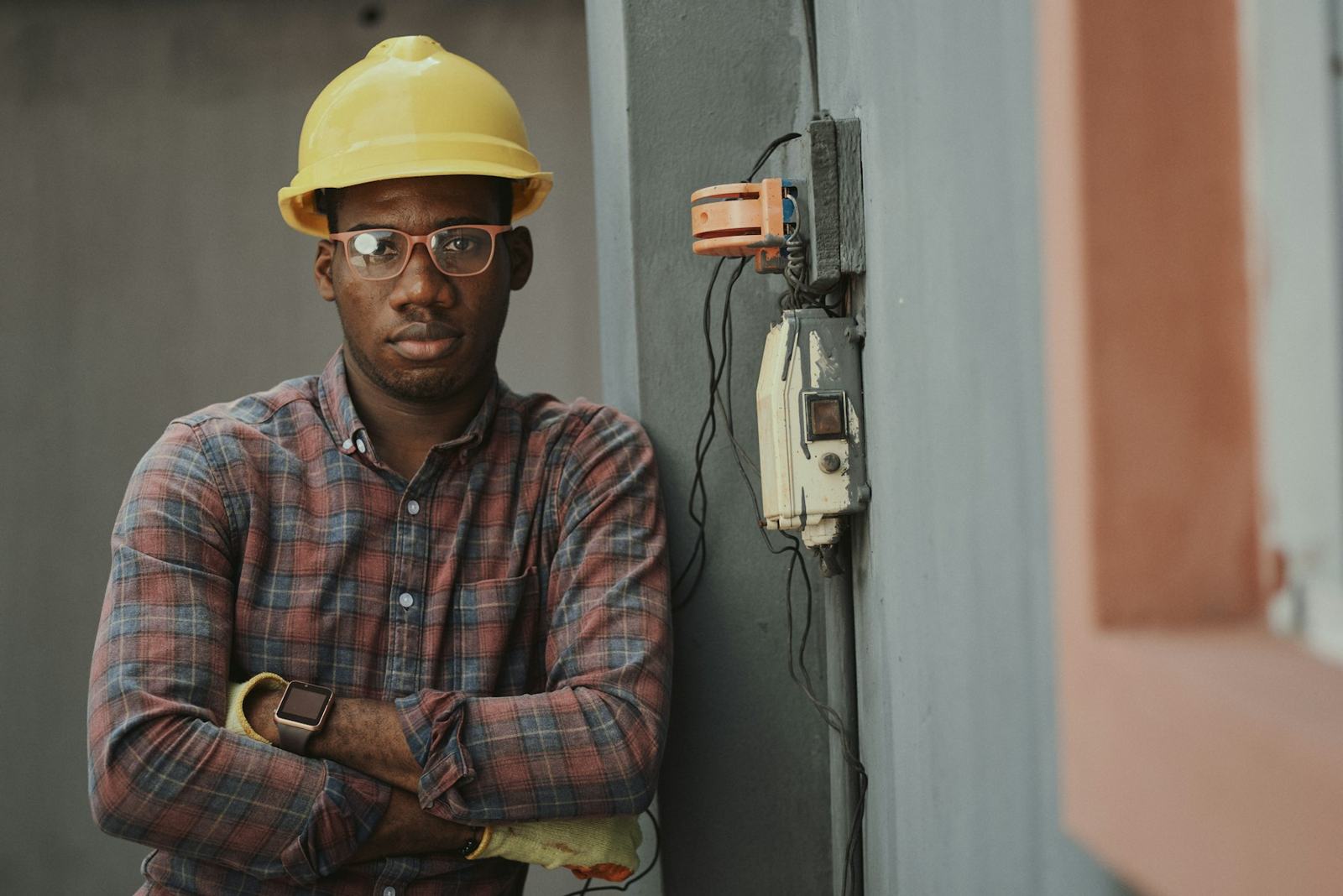Dan Okafor, owner of Ferrule Electrical, standing with arms crossed beside a meter box in his hard hat and glasses