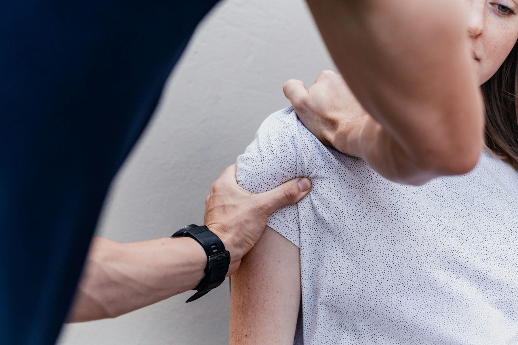A physiotherapist assessing a patient's shoulder with both hands