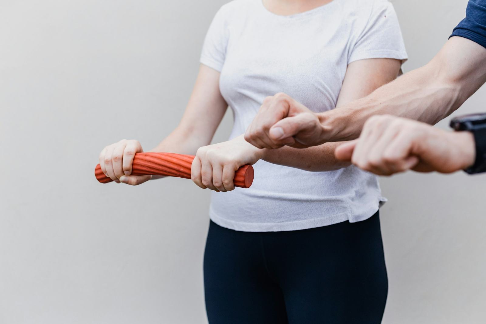 A physiotherapist guiding a woman's arm as she twists an orange flexible rehab bar